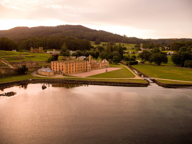 Aerial shot of Port Arthur Historic Site from above the water, showing the sandstone buildings and bush hill in the background