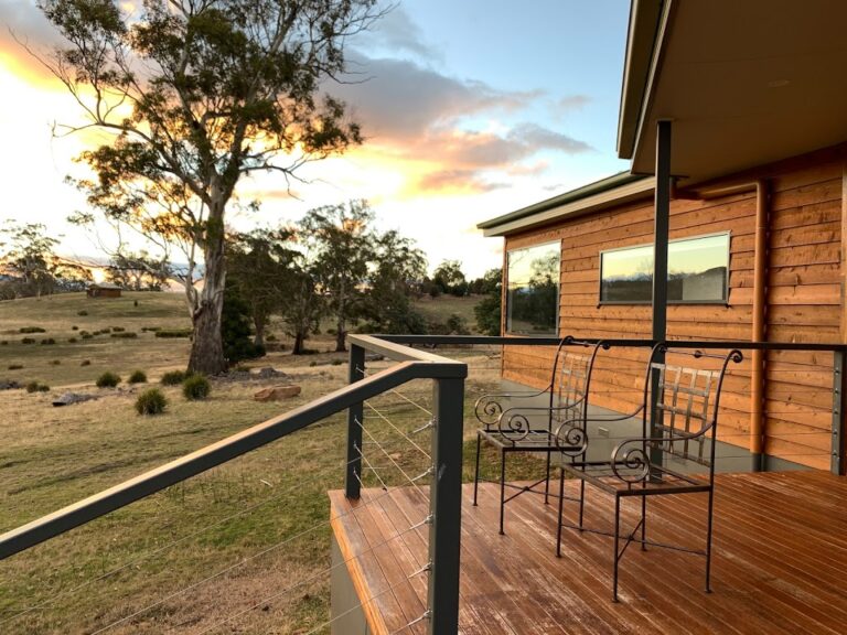 2 Chairs on the balcony of an exposed wooden clad house with a eucalypt tree obscuring the sunset at Curringa Farm